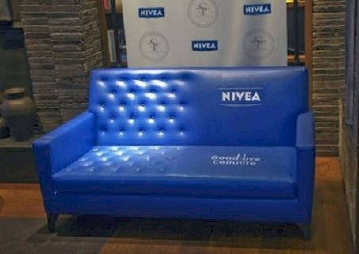 Modrá pohovka, na polovici hladká s logom NIVEA a textom Goodbye cellulite, na druhej polovici prešívaná