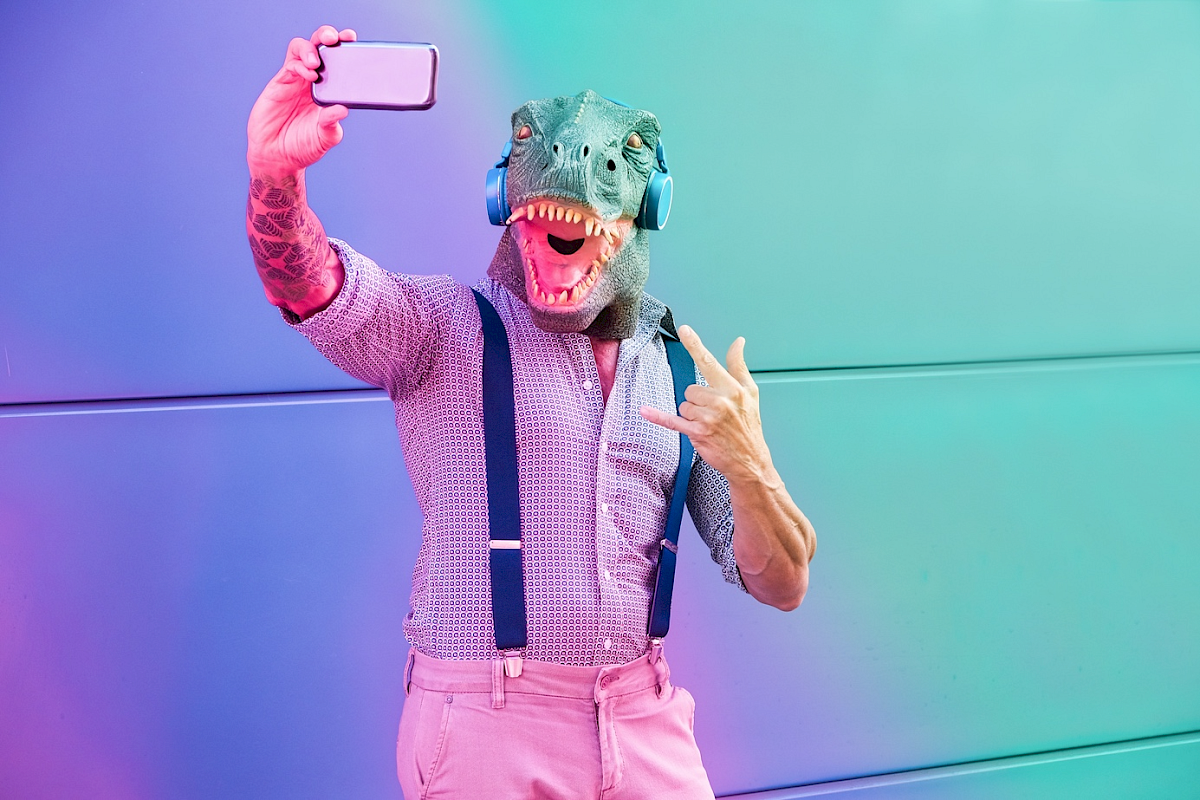 Muž s maskou dinosaura si robí selfie